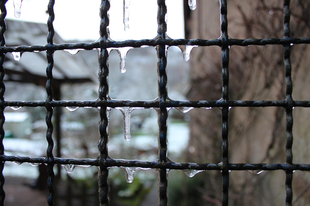 Close view of a black iron grille with icicles hanging from the bars